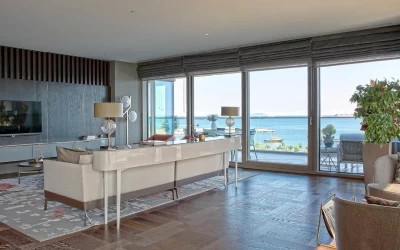 spacious-and-luminous-living-room-with-a-beige-sofa-gray-television-unit-gray-patterned-carpet-and-extensive-sea-view-windows-with-balcony