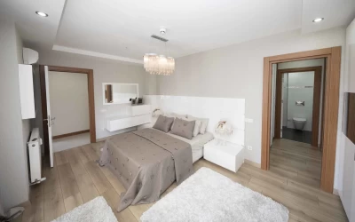 bedroom-with-en-suite-bathroom-furnished-with-double-size-bed-white-furry-carpets-wood-effect-tiles-spot-lights-and-an-elegant-pendant-light
