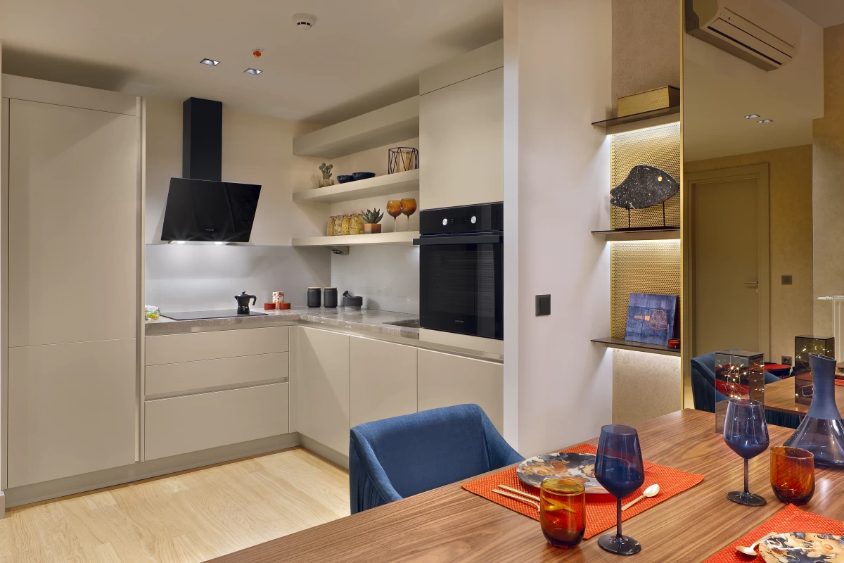 a-modern-kitchen-with-white-kitchen-cabinets-black-built-in-oven-square-dining-tables-two-blue-chairs-and-wine-glasses-on-tables