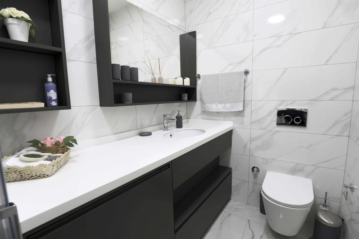 exquisite-bathroom-with-black-and-white-bath-cabinet-soaps-decorative-objects-and-towels-on-it-white-marble-walls-and-a-toilet