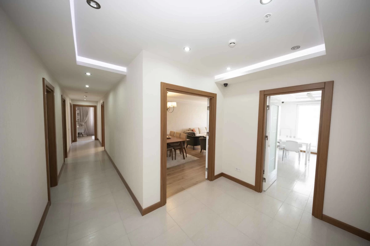 spacious-and-bright-corridor-of-a-residence-with-seven-wooden-doors-a-living-room-and-kitchen-view-from-the-doors