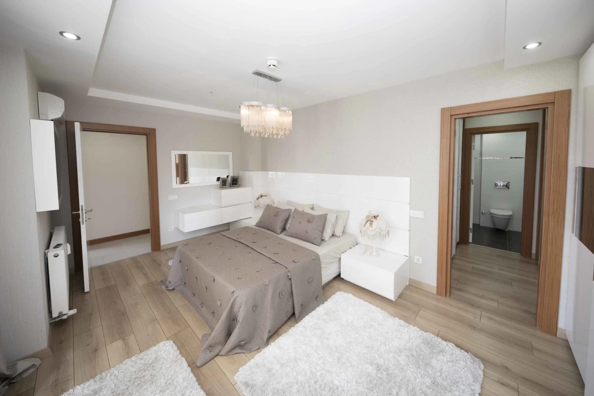 bedroom-with-en-suite-bathroom-furnished-with-double-size-bed-white-furry-carpets-wood-effect-tiles-spot-lights-and-an-elegant-pendant-light