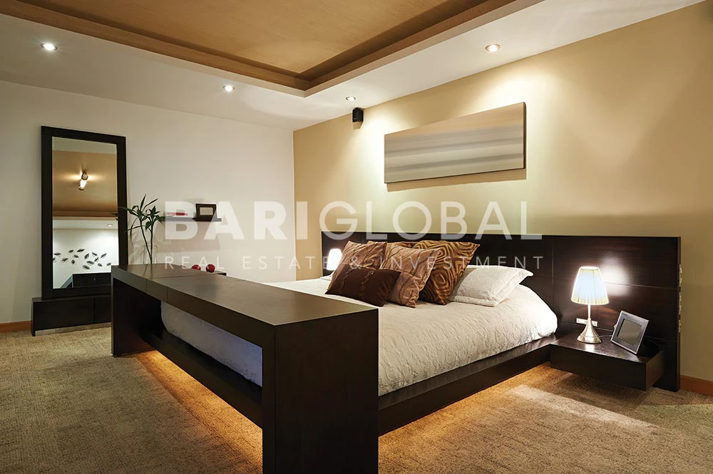 living-room-designed-in-beige-shades-furnished-with-a-double-size-bed-bedside-desks-modern-art-paintings-and-an-en-suite-bathroom